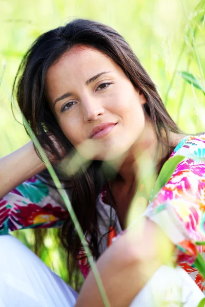 Closeup of beautiful brunette girl sitting in meadow — Stock Photo, Image