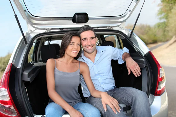 Happy couple sitting in car open trunk — Stock Photo, Image