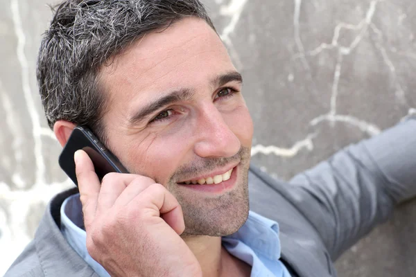 Businessman talking on mobile phone against wall — Stock Photo, Image