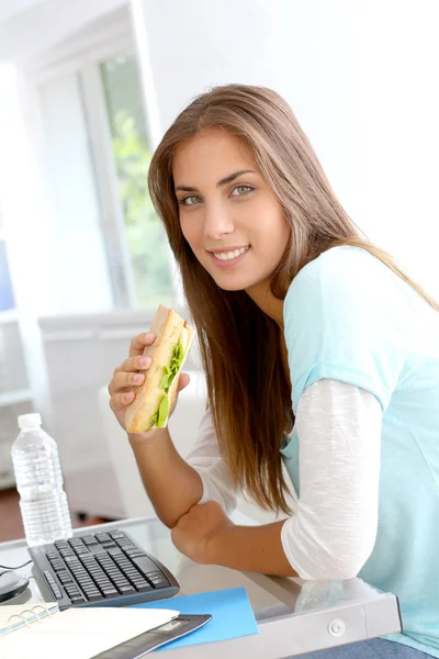 Student Tjej äter smörgås framför skrivbordet — Stockfoto