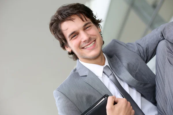 Jeune homme d'affaires souriant assis à l'extérieur du bâtiment — Photo