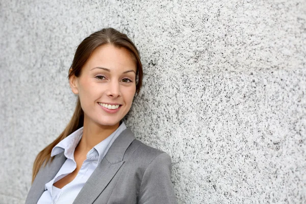 Mulher executiva sorridente apoiando-se na parede cinza — Fotografia de Stock