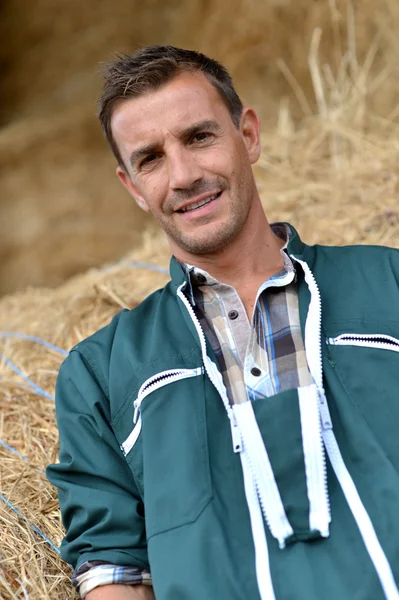 Portret van lachende landbouwer permanent door hooibergen — Stockfoto