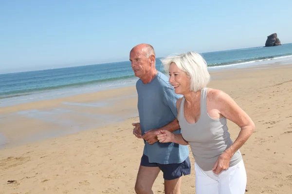 Pareja mayor corriendo en una playa de arena — Foto de Stock