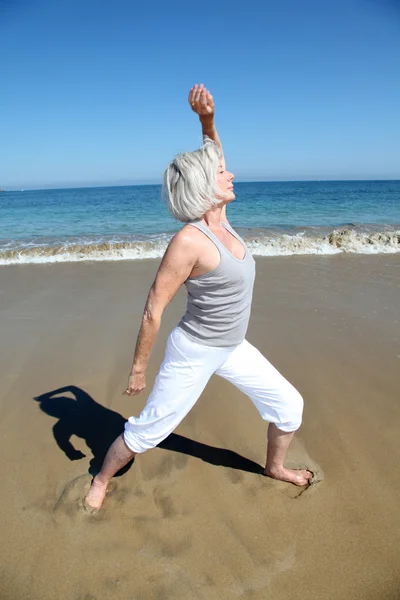 Äldre kvinna gör stretching övningar på stranden — Stockfoto