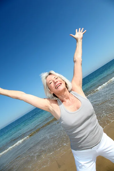 Senior vrouw doen uitrekkende oefeningen op het strand — Stockfoto