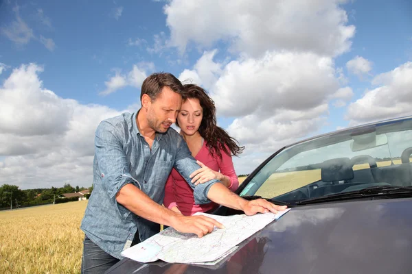 Ehepaar schaut auf Straßenkarte auf Motorhaube — Stockfoto