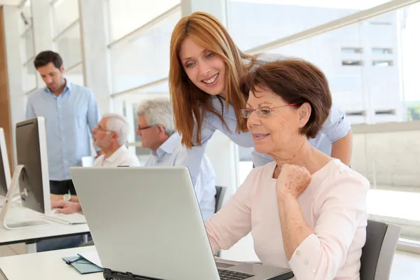 Donna anziana con allenatore davanti al computer portatile — Foto Stock