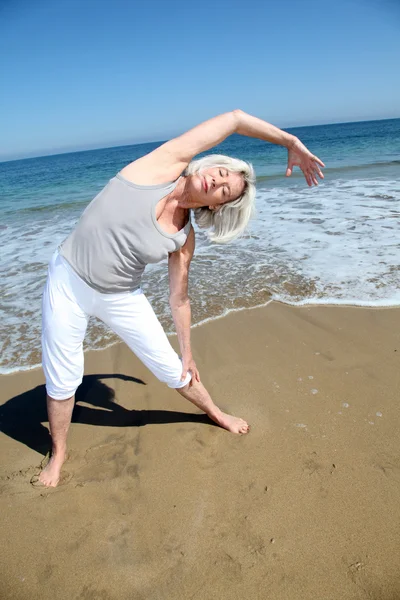 Femeia în vârstă care face exerciții de întindere pe plajă Fotografie de stoc