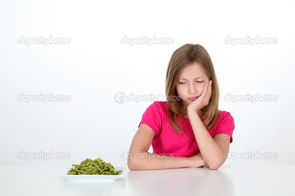 Young girl looking at plate of green beans with disgust
