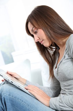 Elektronik pad ile koltuk üzerinde oturan genç kadın