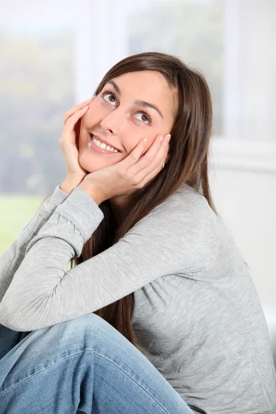 Smiling young woman at home sitting on sofa — Stock Photo, Image