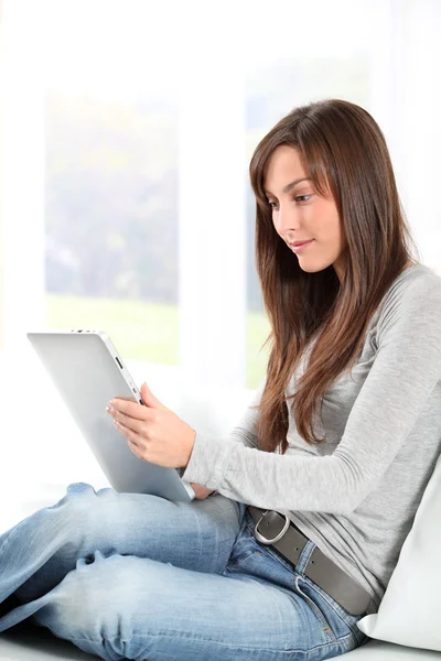 Elektronik pad ile koltuk üzerinde oturan genç kadın — Stok fotoğraf