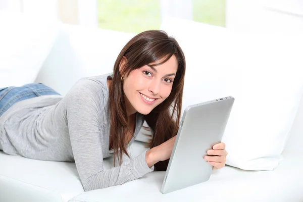 Mujer joven sentada en sofá con almohadilla electrónica — Foto de Stock