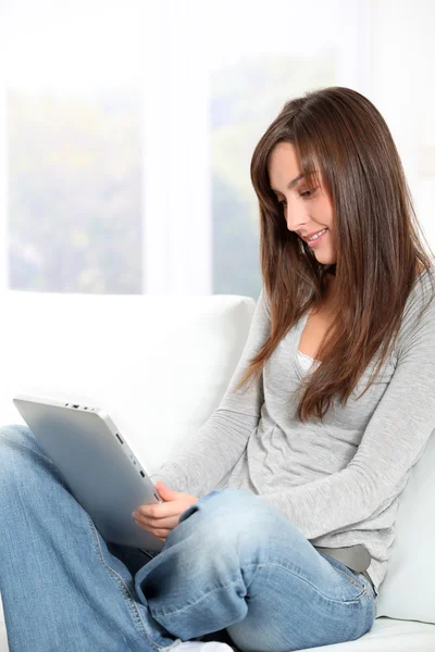 Młoda kobieta siedzi na kanapie z elektronicznych pad — Zdjęcie stockowe