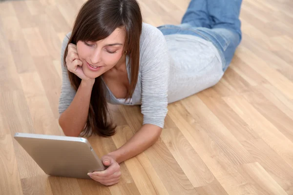 Mujer joven acostada en el suelo con almohadilla electrónica — Foto de Stock