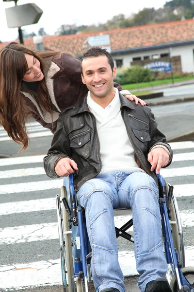 Mulher ajudando amigo em cadeira de rodas atravessar a rua — Fotografia de Stock