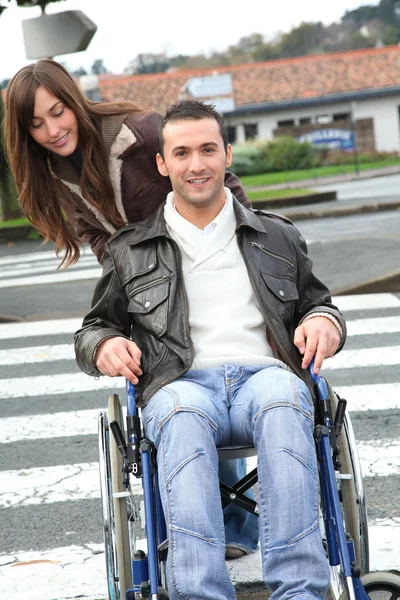 Femme aidant ami en fauteuil roulant traverser la rue — Photo