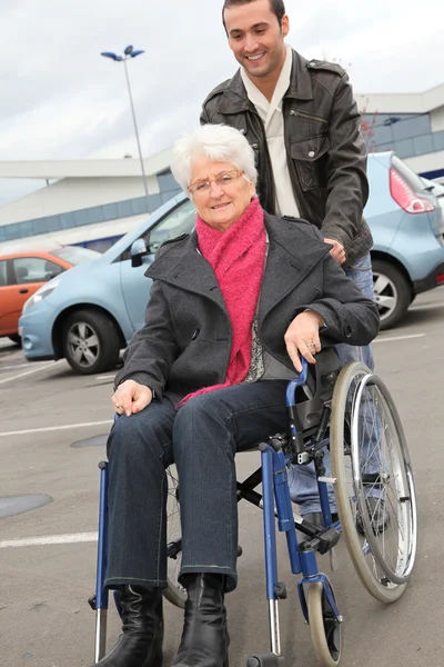 Mladý muž pomáhat starší žena na vozíku — Stock fotografie