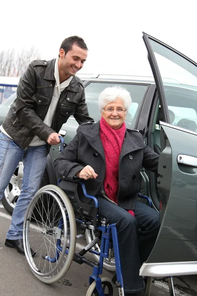 Junger Mann hilft Seniorin im Rollstuhl — Stockfoto