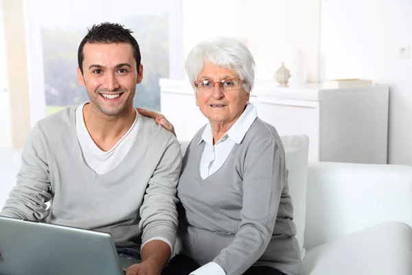 Mujer anciana con hombre joven usando internet en casa — Foto de Stock