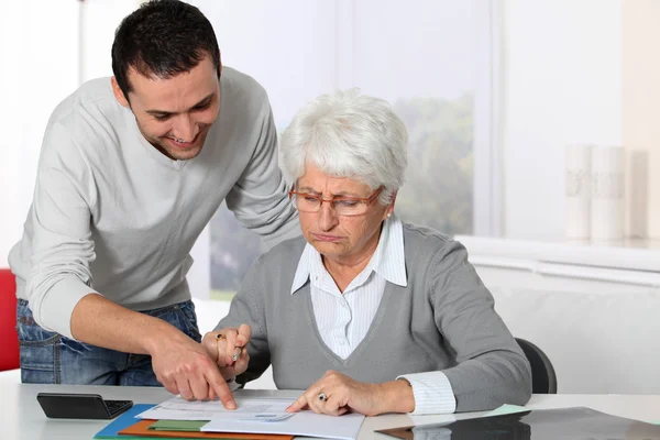 Young man helping elderly woman with paperwork — Stock Photo, Image