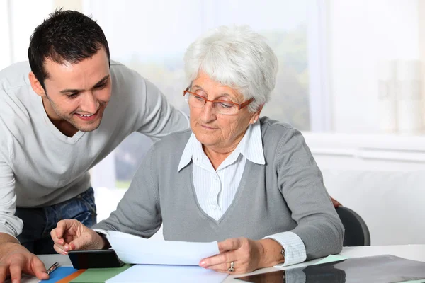 A fiatalember segít idős nő a papírmunka — Stock Fotó