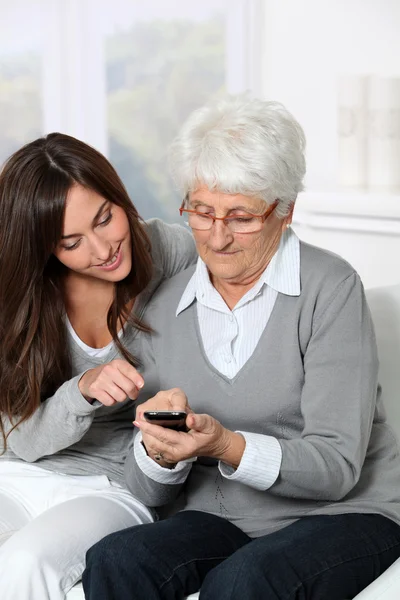 Mujer joven mostrando cómo utilizar el teléfono móvil a la abuela — Foto de Stock