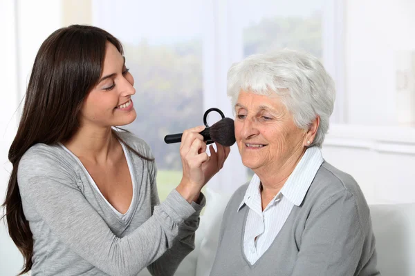 Young woman helping old woman to put makeup on — Stock Photo, Image