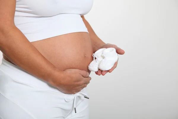 Pregnant woman belly with newborn slippers — Stock Photo, Image