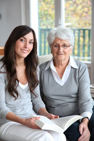 Young woman reading book to elderly woman Stock Image