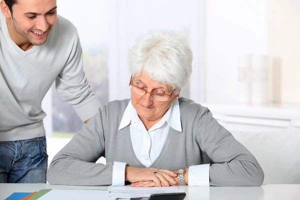 Young man helping elderly woman with paperwork — Stock Photo, Image