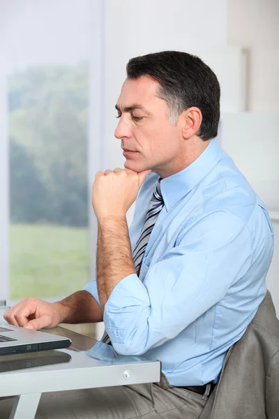 Zakenman zit aan zijn bureau met hand op kin — Stockfoto