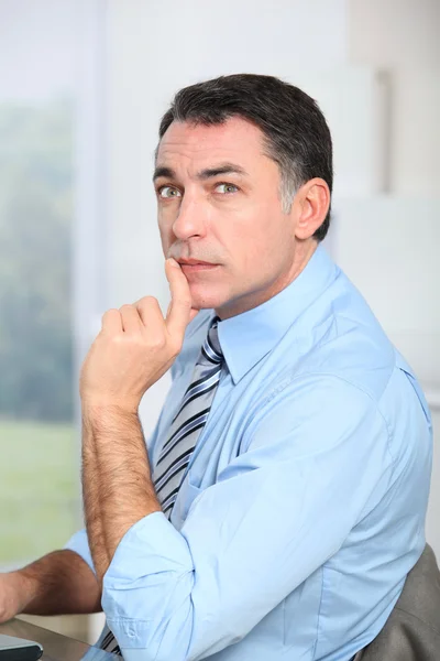 Zakenman zit aan zijn bureau met hand op kin — Stockfoto