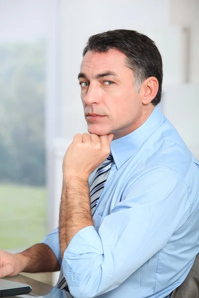 Geschäftsmann sitzt mit der Hand am Kinn am Schreibtisch — Stockfoto