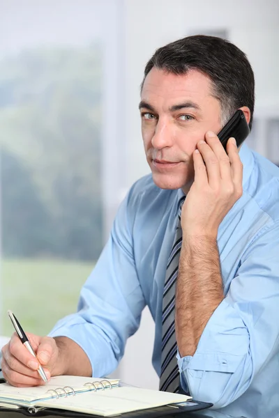 Uomo d'affari al telefono che scrive in agenda — Foto Stock