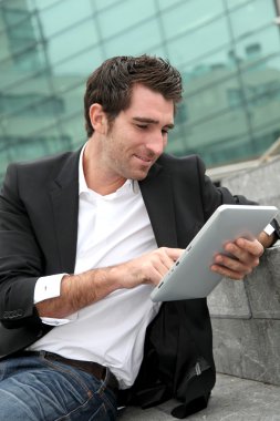 Modern binanın önünde elektronik tablet kullanan bir adam.