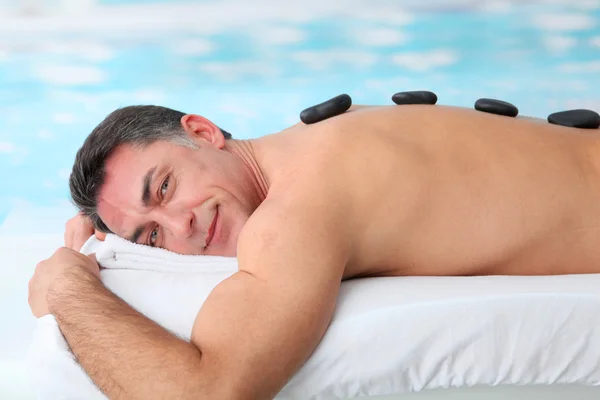 Hombre acostado en cama de masaje con piedras calientes — Foto de Stock