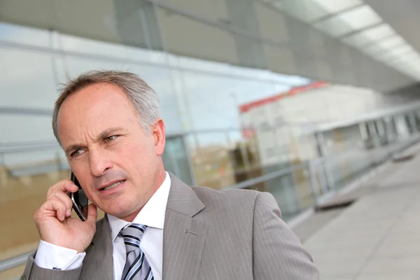 Empresário com telefone celular na frente do edifício moderno — Fotografia de Stock