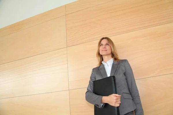 Businesswoman standing in hall against wall — Stock Photo, Image
