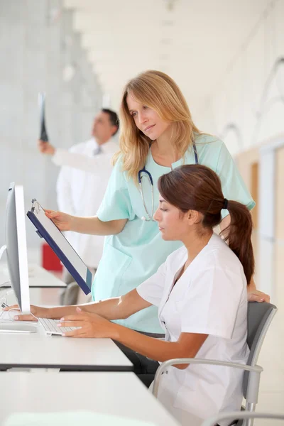 Verpleegster met intern werken achter computer — Stockfoto