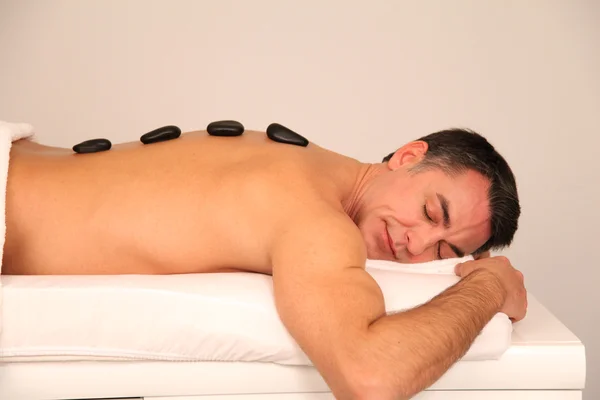 Man laying on massage bed with hot stones on his back — Stock Photo, Image