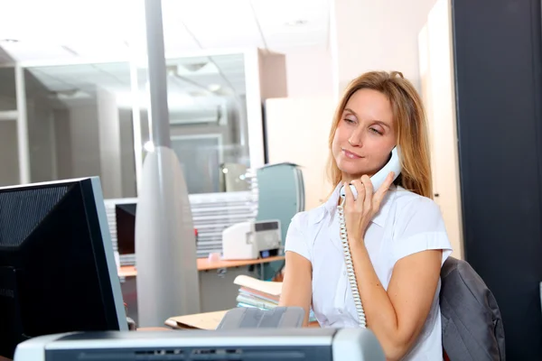 Mulher loira falando ao telefone na frente do computador de mesa — Fotografia de Stock