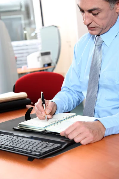 Businessman at his desk writing down on his agenda — Stock Photo, Image