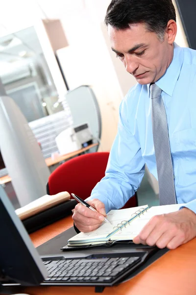 Affärsman vid sitt skrivbord skriva ner på hans dagordning — Stockfoto