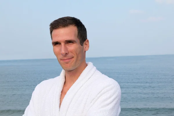 Smiling man standing by the sea in bathrobe — Stock Photo, Image