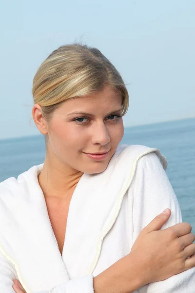 Smiling beautiful woman standing by the sea in bathrobe — Stock Photo, Image