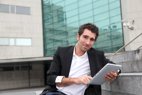 Modern binanın önünde elektronik tablet kullanan bir adam.