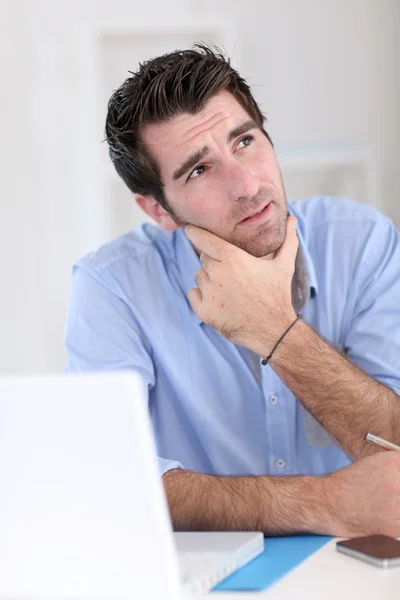 Office worker with thoughtful look in front of laptop — Stock Photo, Image