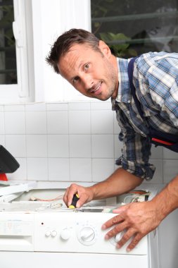 Tesisatçı bozuk çamaşır makinesini tamir ediyor.